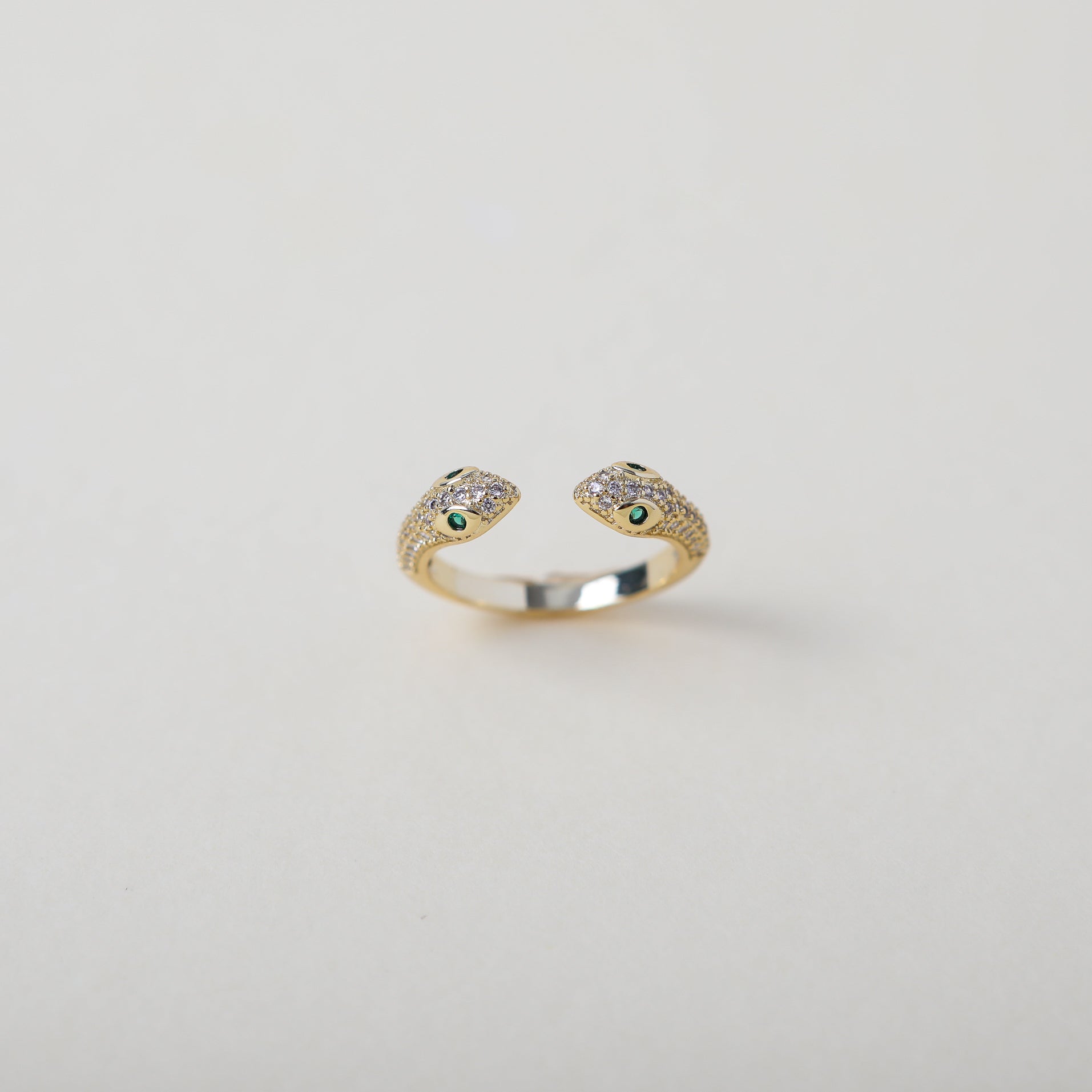 Gold and crystal accented open claw ring featuring two snake heads with green crystal eyes green eyes