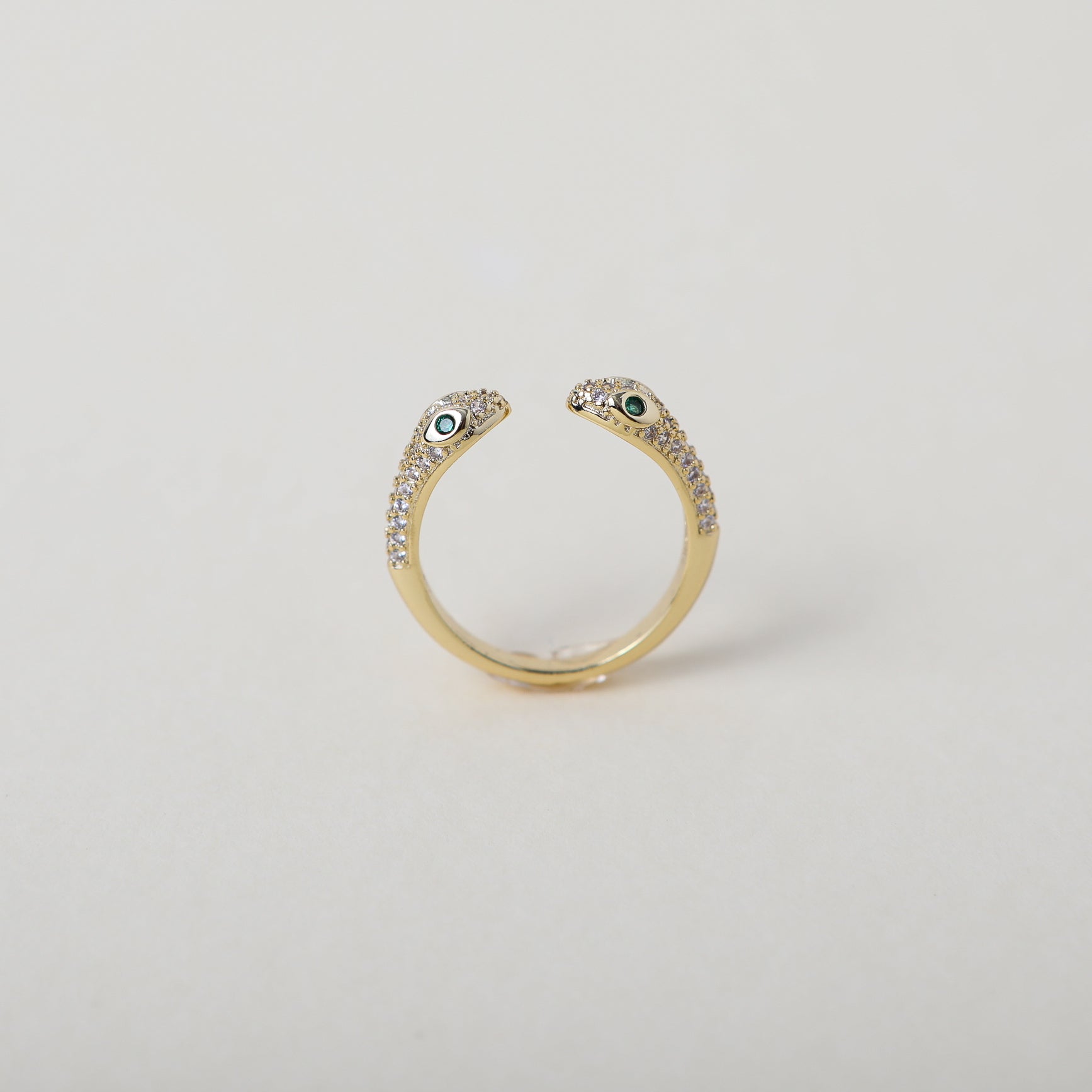 Gold and crystal accented open claw ring featuring two snake heads with green crystal eyes green eyes